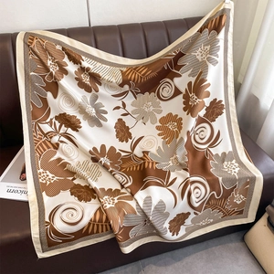 Detail of silk square scarf featuring floral patterns draped on a brown leather sofa