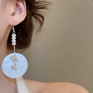 Close-up of elegant long pearl earrings with silver disk charms on a female model