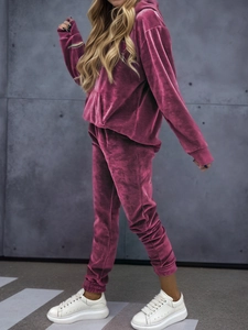 Detail of a dark pink velvet tracksuit featuring a hoodie and joggers in a street setting