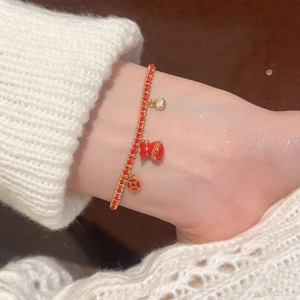 Detail of red cord bracelet with gold lucky bag and copper coin charms on wrist