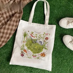 Close-up of cream canvas tote bag with vintage vegetable illustrations on green grass