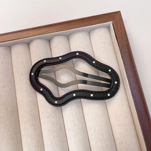 Macro shot of wavy black PU leather hair clip with white dots on a beige velvet tray