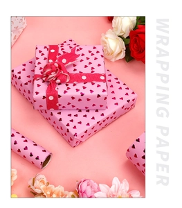 Close-up of pink wrapping paper with shiny red gold hearts and wrapped gift box