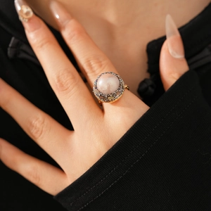 Macro shot of gold vintage ring with pink pearl and pavé diamonds on finger