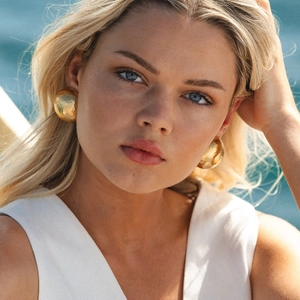 Detail of round hammered gold earrings on female model with a sunny beach background