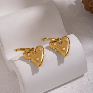 Détail de boucles d'oreilles cœur doré irrégulier avec perles sur support en pierre