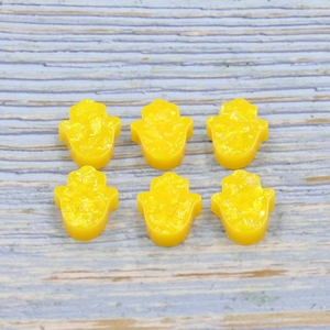 Macro shot of six yellow resin Hamsa Hand charms with glitter detail on wood