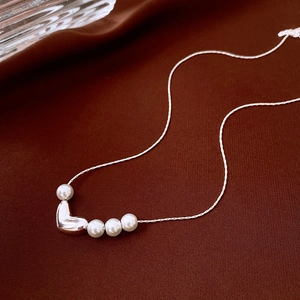 Detail of silver heart pendant pearl necklace on elegant dark silk fabric background