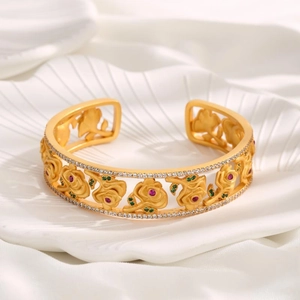 Detailed shot of a gold-plated flower bangle with red and green gems on a shell tray