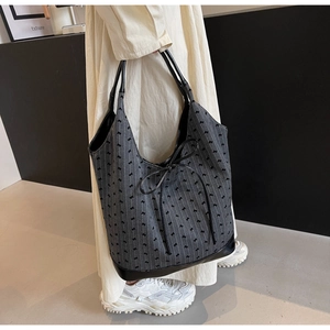 Detail of grey striped tote bag featuring black leather base and decorative bow accent