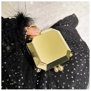 Detail of a golden octagonal mirror metal clutch bag held in a fashionable evening setting