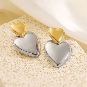 Minimalist gold and silver two-tone heart drop earrings on a beige stone surface