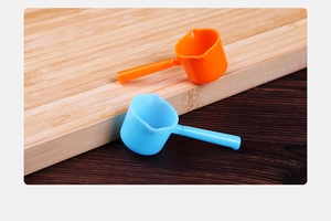 Close-up of orange and blue plastic measuring spoons on a rustic wooden cutting board
