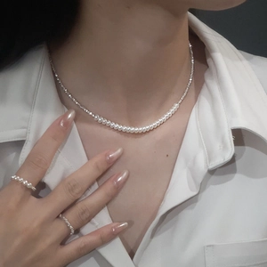 Close-up of S925 sterling silver pearl necklace and rings on a white shirt