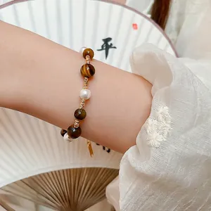 Tiger eye stone and pearl beaded bracelet with gold plating on a fan background
