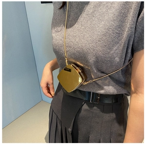 Mini gold glossy metallic shoulder bag with chain strap worn by a model as a crossbody accessory