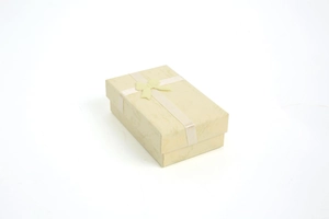 Macro shot of rectangular beige jewelry box with white satin ribbon and bow detailing