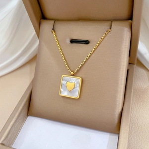 Gold square shell pendant necklace with heart detail in a beige jewelry box