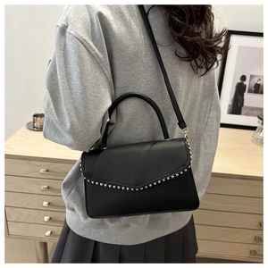 Detail view of a black faux leather handbag featuring silver studs and top handle