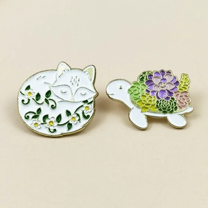 Detail of enamel pins featuring a sleeping fox and a turtle with succulent floral patterns