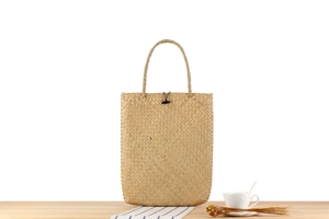 Detail of woven straw tote bag with round handles, black button and decorative props