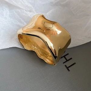 Macro shot of irregular wavy gold-plated wide cuff bracelet with mirror finish