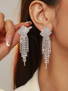 Close-up of sparkling square rhinestone earrings with long silver tassels on a model