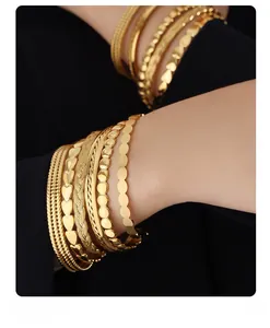 Close-up of stacked gold 18k bracelets with heart and twisted rope textures on a wrist