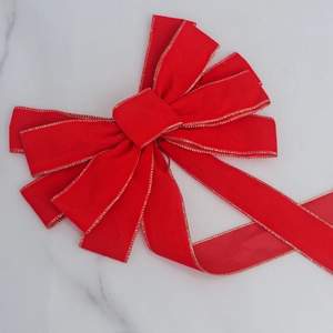 Close-up of red velvet Christmas bow with gold wire edges on white marble surface
