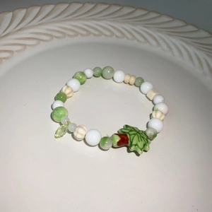 Détail du bracelet en perles macaron avec pendentif feuille verte et pierres œil de chat