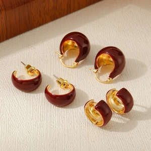 Macro detail of three pairs of vintage deep red enamel gold earrings on a textured background