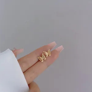 Close-up of golden butterfly earrings with matte finish held by hand on grey background