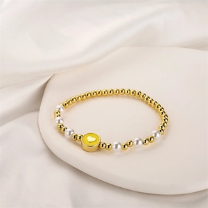 Détail du bracelet élastique avec perles dorées et pendentif en forme de cœur jaune