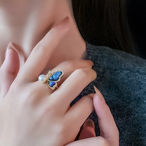 Close-up of gold butterfly ring with blue shell wings and white freshwater pearl detail