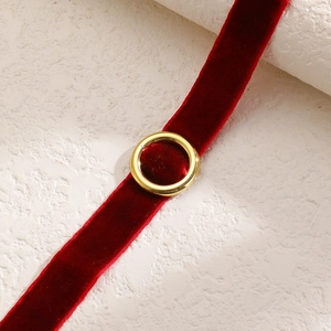Dettaglio del choker in velluto rosso con anello dorato su sfondo strutturato neutro