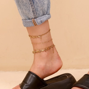 Layered gold anklet set with heart charm and anchor chains on model's ankle