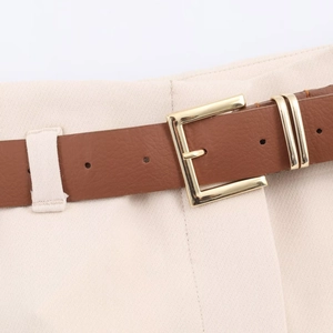 Macro view of a classic brown leather belt with a textured gold square pin buckle on trousers
