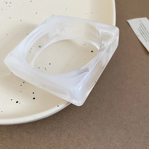 Minimalist white translucent acrylic square bangle with smooth geometric edges on a plate