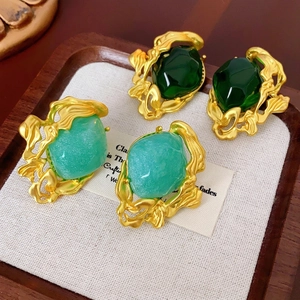 Vintage emerald stud earrings with liquid gold textured borders on a wooden tray