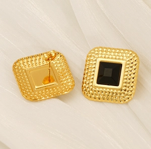 Macro detail of gold vintage square studs featuring black stones and textured metal edges