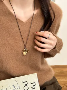 Detail view of a golden irregular pendant necklace on a brown sweater with a grid-textured ring