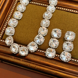 Detailed view of silver necklace and earring set with round rhinestones in wooden frame