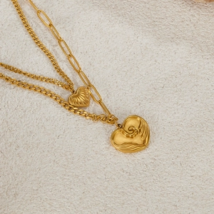 Detail of layered gold heart necklace featuring paperclip chain and embossed charms
