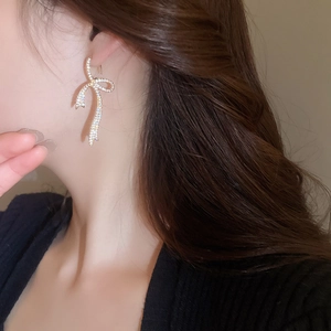 Close-up of gold-plated ribbon bow earring with shimmering zircons worn by a model