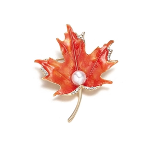 Macro shot of maple leaf brooch with orange enamel, center pearl, and rhinestone details