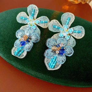 Close-up of blue beaded floral earrings with yarn embroidery and rhinestone details