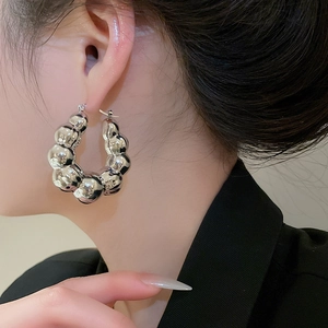 Close-up of a model wearing large silver polished beaded hoop earrings in a minimalist style