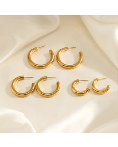 Detailed view of three pairs of thick polished gold C-shaped hoop earrings on satin fabric
