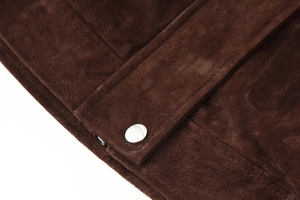 Nahaufnahme einer dunkelbraunen Wildlederjacke mit weicher Textur und silbernem Metallknopf