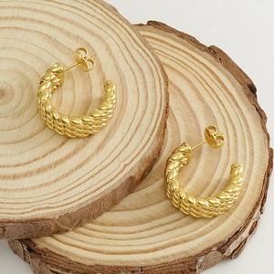 Modern twisted C-shape hoop earrings in 18k gold-plated stainless steel on a wood surface